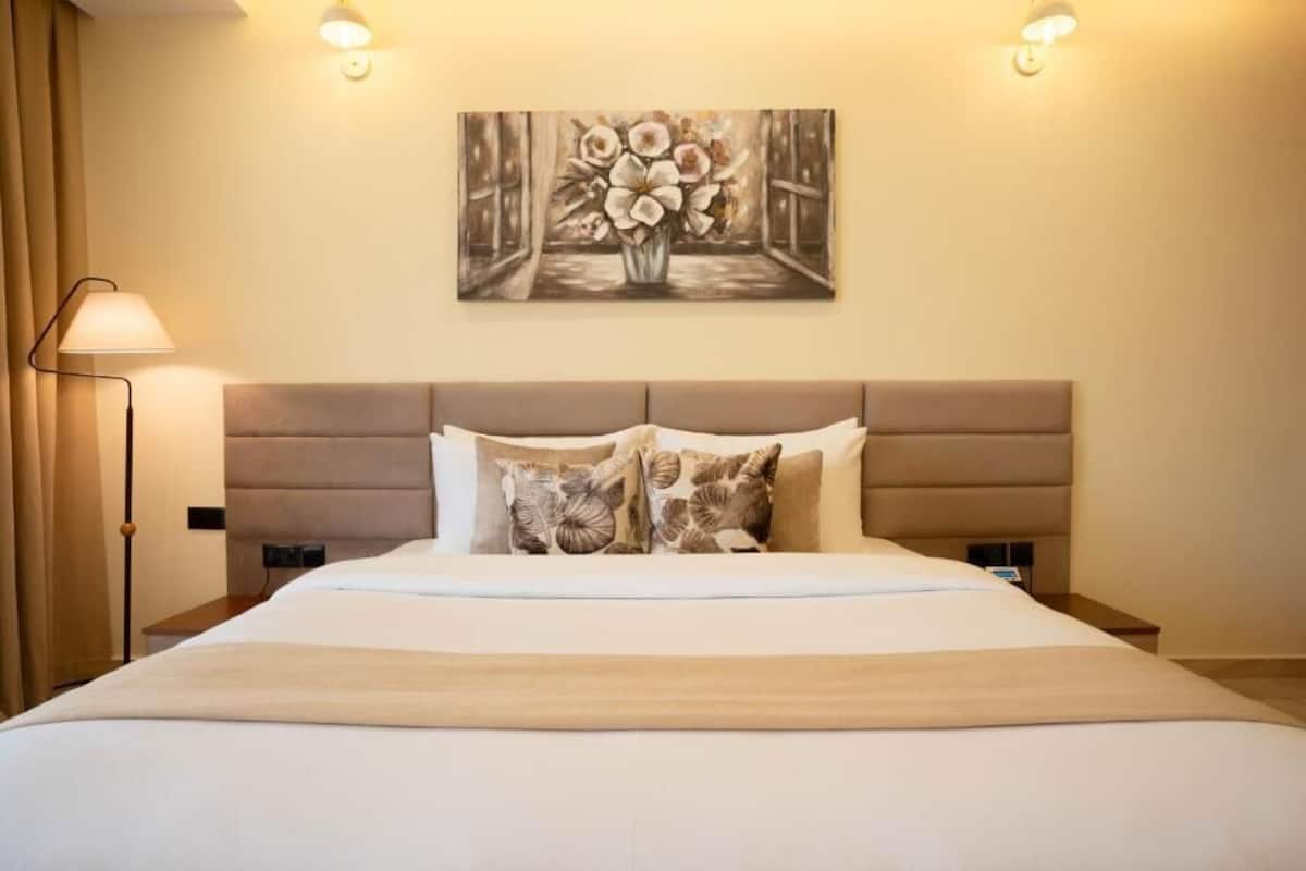 Une chambre d’hôtel avec un grand lit, une tête de lit, deux lampes de chevet, une table de chevet et un tableau accroché au mur.