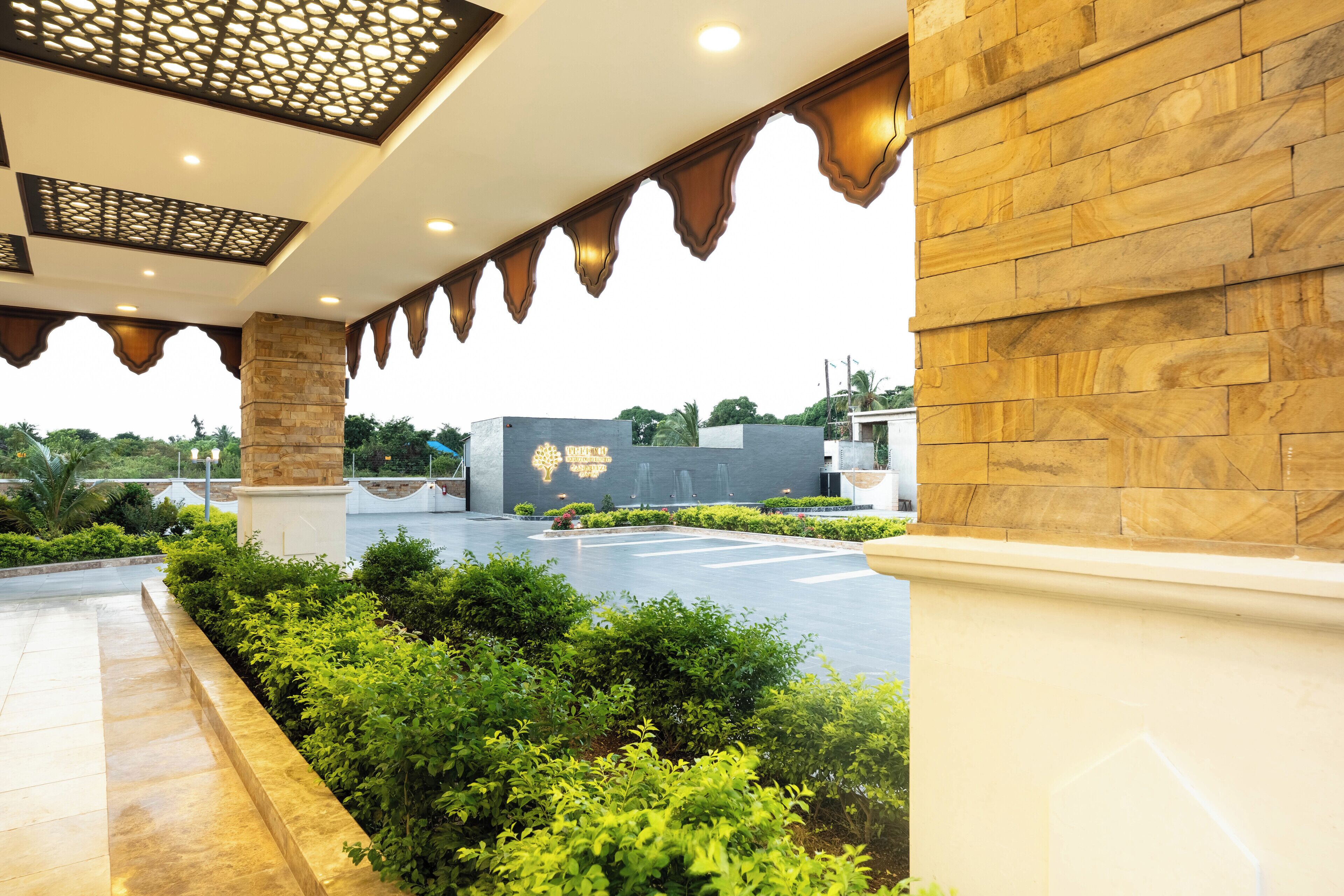 A covered outdoor area with stone columns, a paved walkway, and greenery.