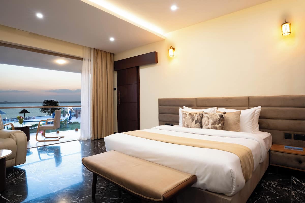 Une chambre d’hôtel moderne dotée d’un grand lit, d’une banquette, d’une vue sur la mer et d’un balcon avec des sièges d’extérieur.