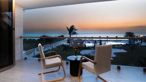 A balcony with two chairs and a table, overlooking a scenic view of the ocean and a distant shoreline with buildings and palm trees. - Treetop by Eight Continents, Zanzibar (Unguja Ukuu)