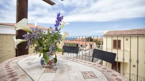 A round table with a patterned tablecloth, a potted plant with flowers, and a view of buildings and a railing. - Casa 10 Da Georgette - Affitti Brevi Italia (Valledoria)