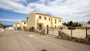 A residential street with houses, a stone wall, and a metal gate. - Casa 10 Da Georgette - Affitti Brevi Italia (Valledoria)