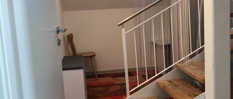 A staircase with wooden steps and metal railings, leading to a landing with a red carpet.