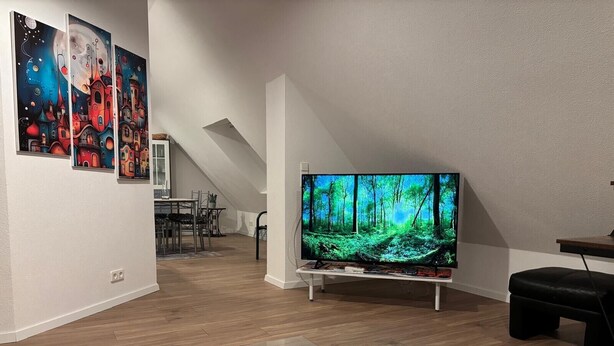 A modern living room with a flat-screen TV, a dining area, and artwork on the walls. - Aurora Lodge (92 m²) with Balcony and Wi-Fi (Engstingen)