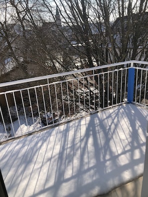 Un balcon enneigé, doté d’une rambarde en métal blanc et d’un poteau bleu.