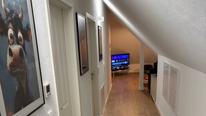 A hallway with wooden flooring, white walls, and a mounted TV in the background. - Aurora Lodge (92 m²) with Balcony and Wi-Fi (Engstingen)