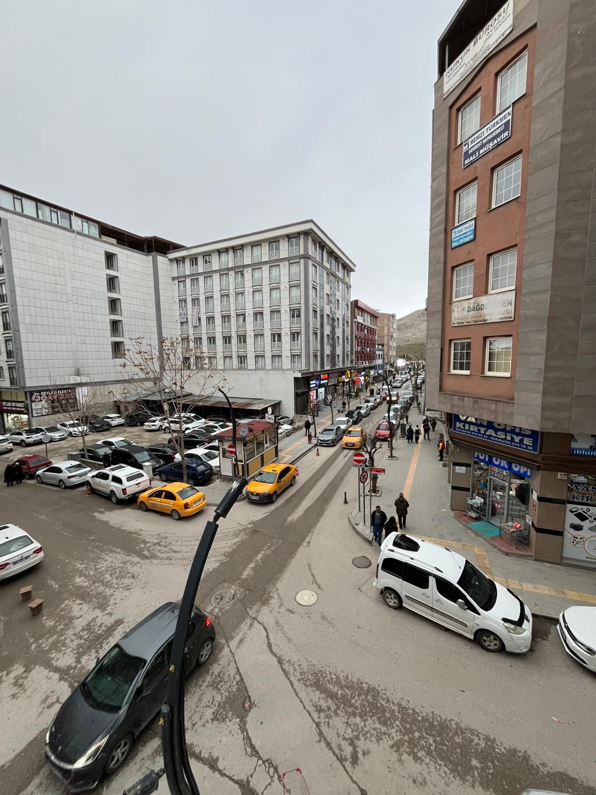 Katunäkymä, jossa on parkkeerattuja autoja, pakettiauto ja rakennus, jossa on useita ikkunoita ja kylttejä.