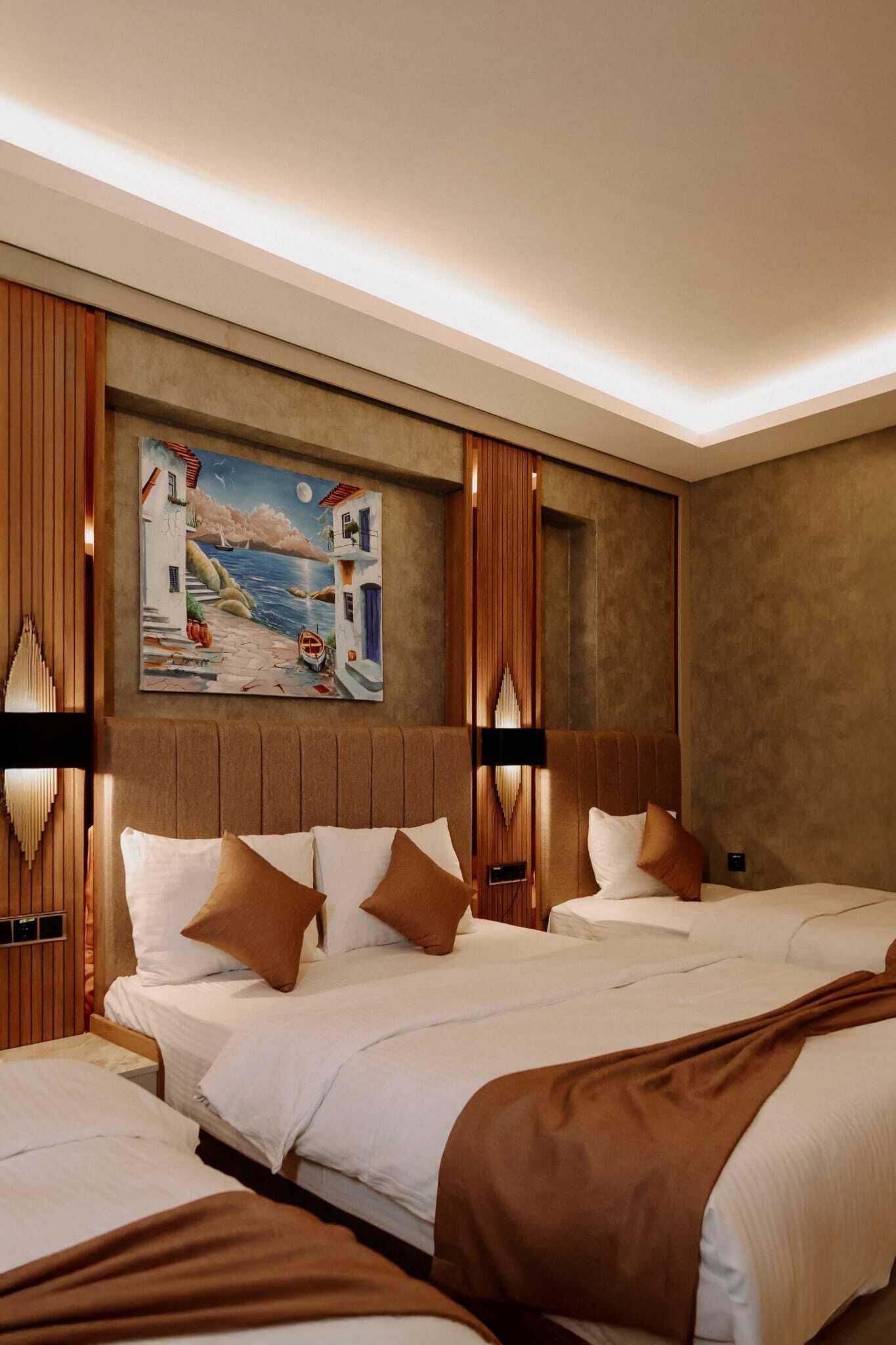 A hotel room with a large bed, a smaller bed, a painting of a coastal scene, and a wooden headboard.