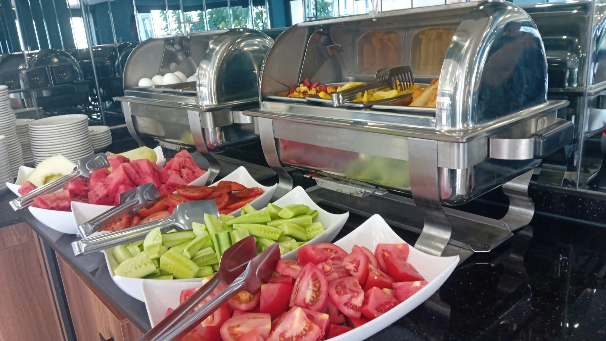 Un bufé con diversas opciones de comida, incluyendo tomates en rodajas, pepinos y sandía.