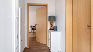 A hallway with a wooden door, a white cabinet with a lamp, and a dining area in the background.