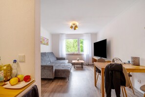 Una sala de estar con sofá, mesa de comedor, televisor y ventana con vista a árboles.