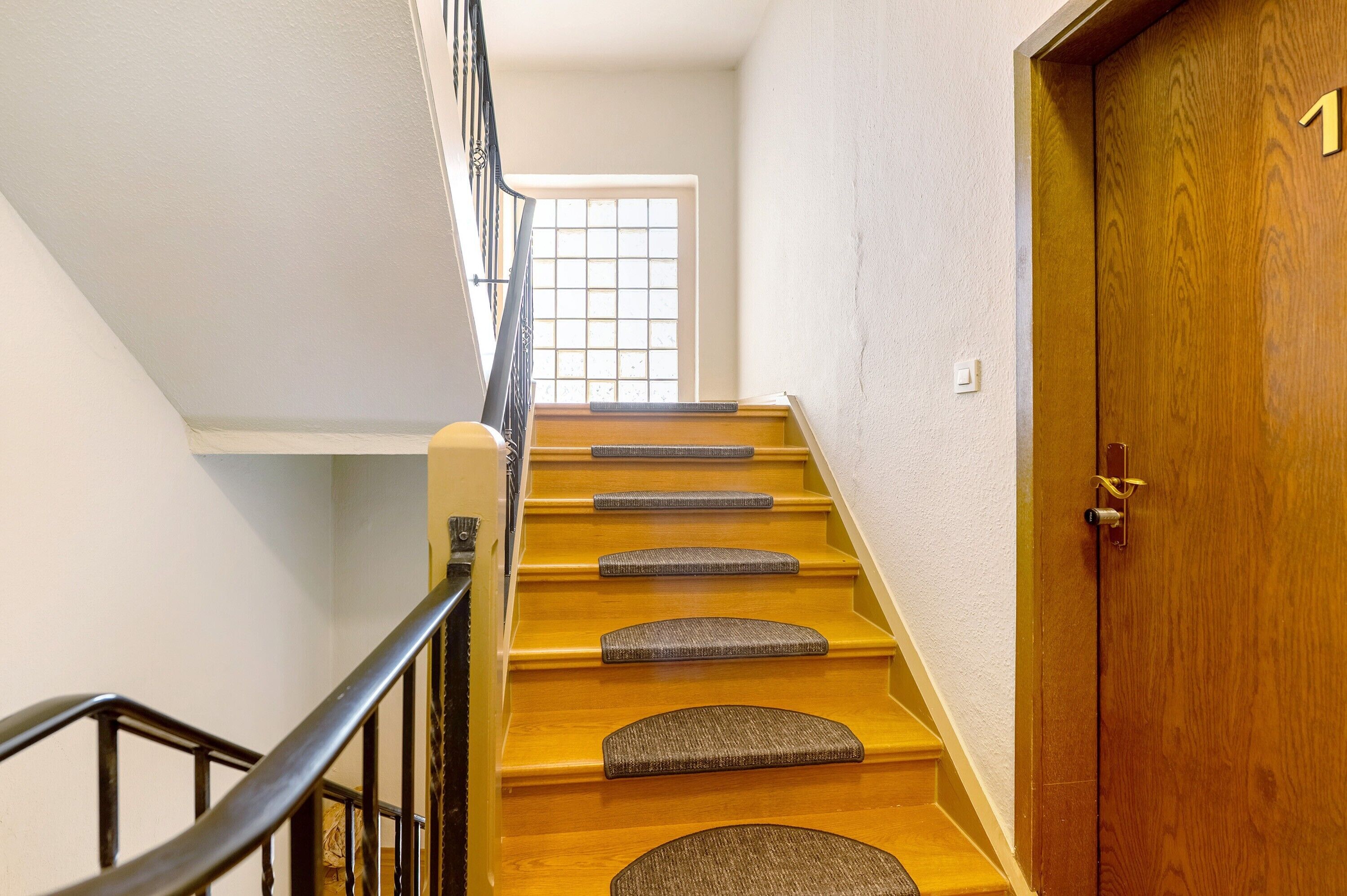 Eine Holztreppe mit Geländern, eine Tür mit einer Nummer und ein Fenster mit Gittermuster.