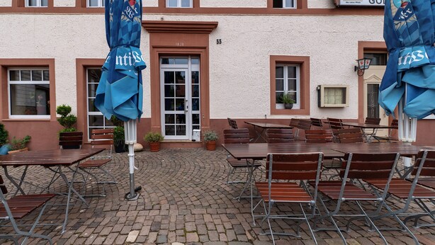 An outdoor patio with tables and chairs, a building with a sign reading 'Park Golf,' and a door with the number 18.38. - Apartment '7' with Air Conditioning, Shared Garden and Wi-Fi (Thaleischweiler-Fröschen)