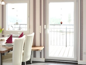 Un comedor con una mesa lista para dos personas, una puerta corrediza de vidrio que da a un balcón y vistas al exterior.