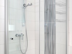 A glass-enclosed shower with a chrome showerhead and control panel, a clear glass door, and a metal shelf unit on the wall. - Apartment 'Bock Feldmannshof' with Balcony and Wi-Fi (Drolshagen)
