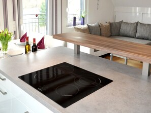 Una cocina moderna con una placa de inducción integrada, una mesa de comedor de madera y un sofá al fondo.