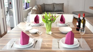 A dining area with a wooden table set for two, a vase with flowers, and two wine bottles.