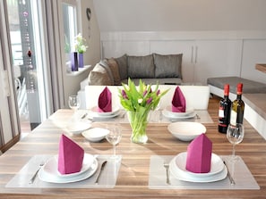 Comedor con mesa de madera dispuesta para dos personas, un jarrón con flores y dos botellas de vino.