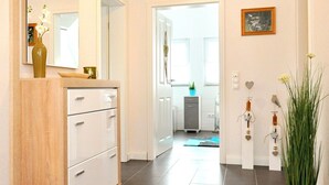 A hallway with a wooden cabinet, a mirror, a vase with flowers, a potted plant, and a door leading to a bathroom.