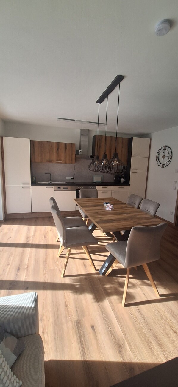 A modern kitchen with wooden cabinets, a dining table with chairs, and a built-in oven.