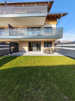 A two-story building with a balcony, a patio area with outdoor furniture, and a well-maintained lawn.