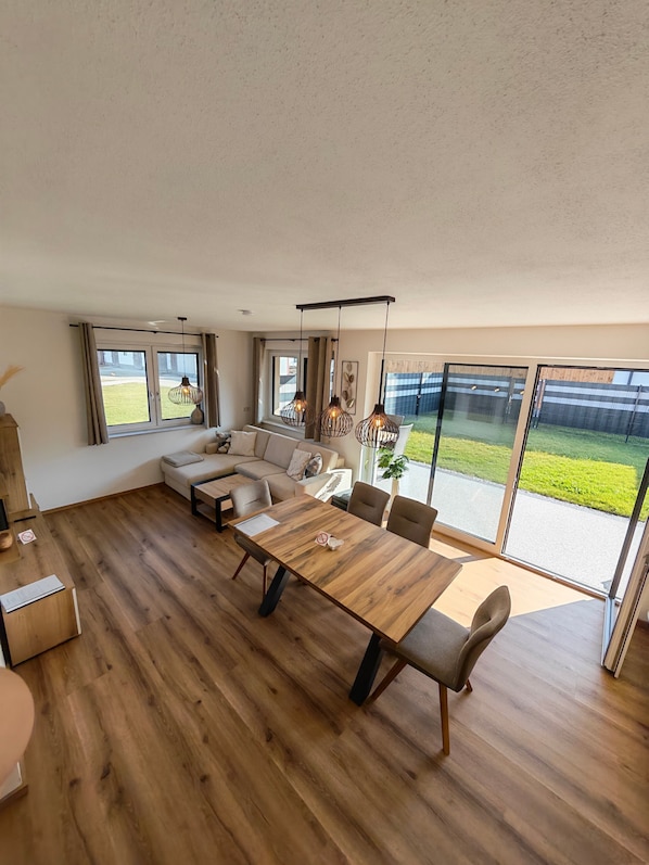 Una sala de estar moderna con piso de madera, una gran mesa de comedor y un conjunto de sofás.