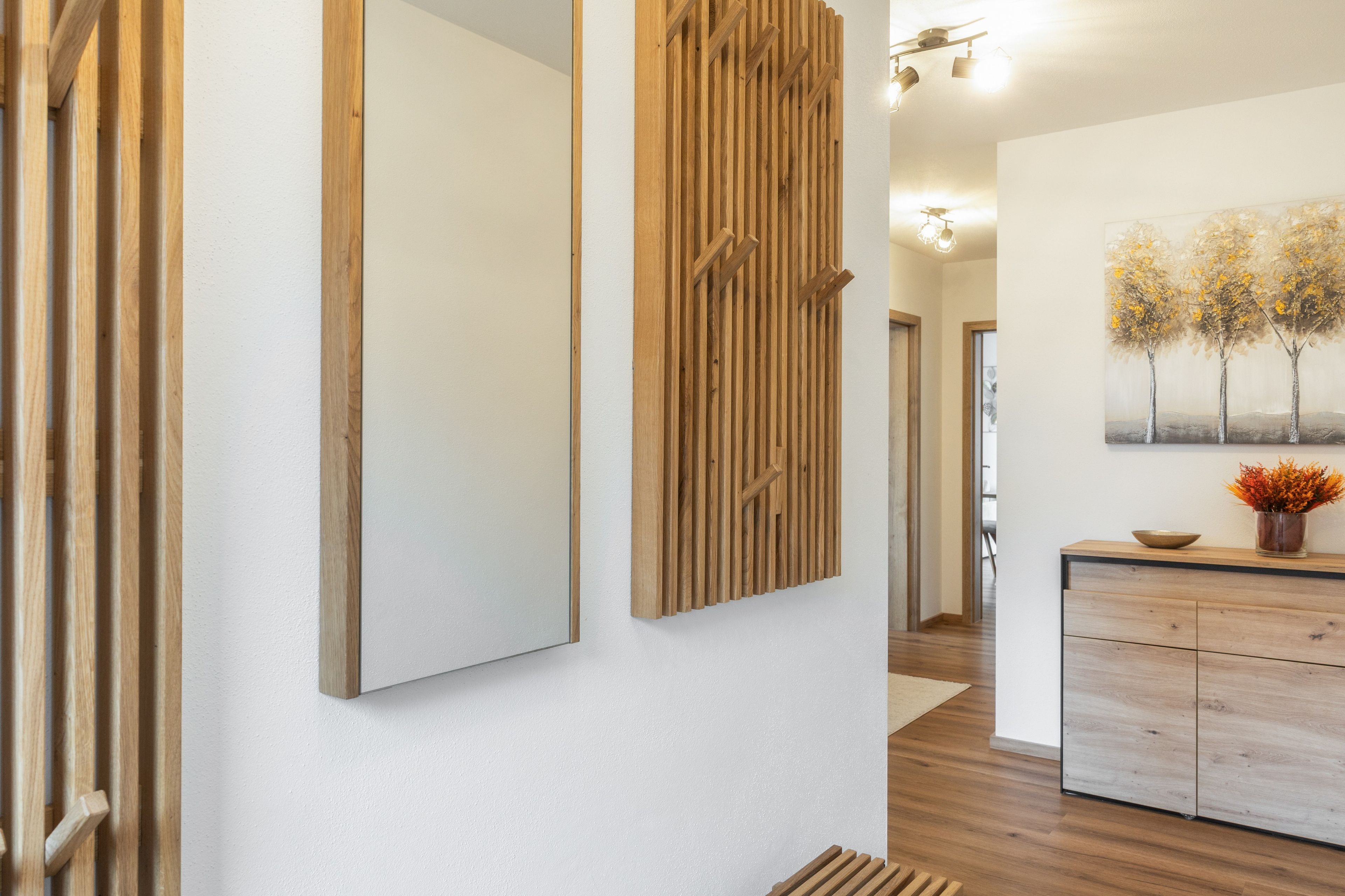 Ein modernes Interieur mit einer Holzwandverkleidung, einem großen Spiegel und einem Baumgemälde.