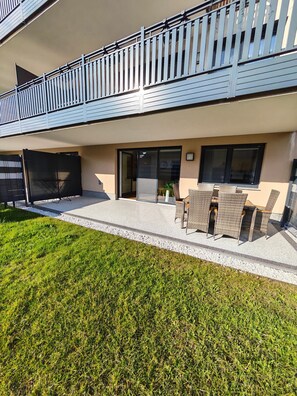A modern building with a balcony, a covered outdoor seating area, and a well-maintained lawn.