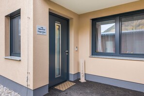 L’entrée d’un immeuble, avec une porte portant l’inscription « Appartement PruggernGlück » et une fenêtre donnant sur une montagne.