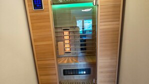 Een sauna met een houten buitenkant, een digitaal bedieningspaneel en een glazen deur.