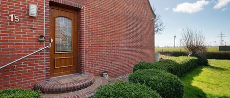 A red brick building with a wooden door, numbered 15, and a small garden with hedges.