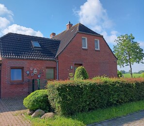 Une maison en briques avec un toit en tuiles, un petit jardin et une haie.