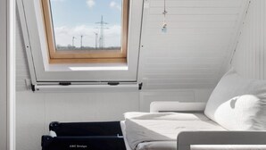 A room with a skylight, a bed, a hanging ornament, and a view of wind turbines.