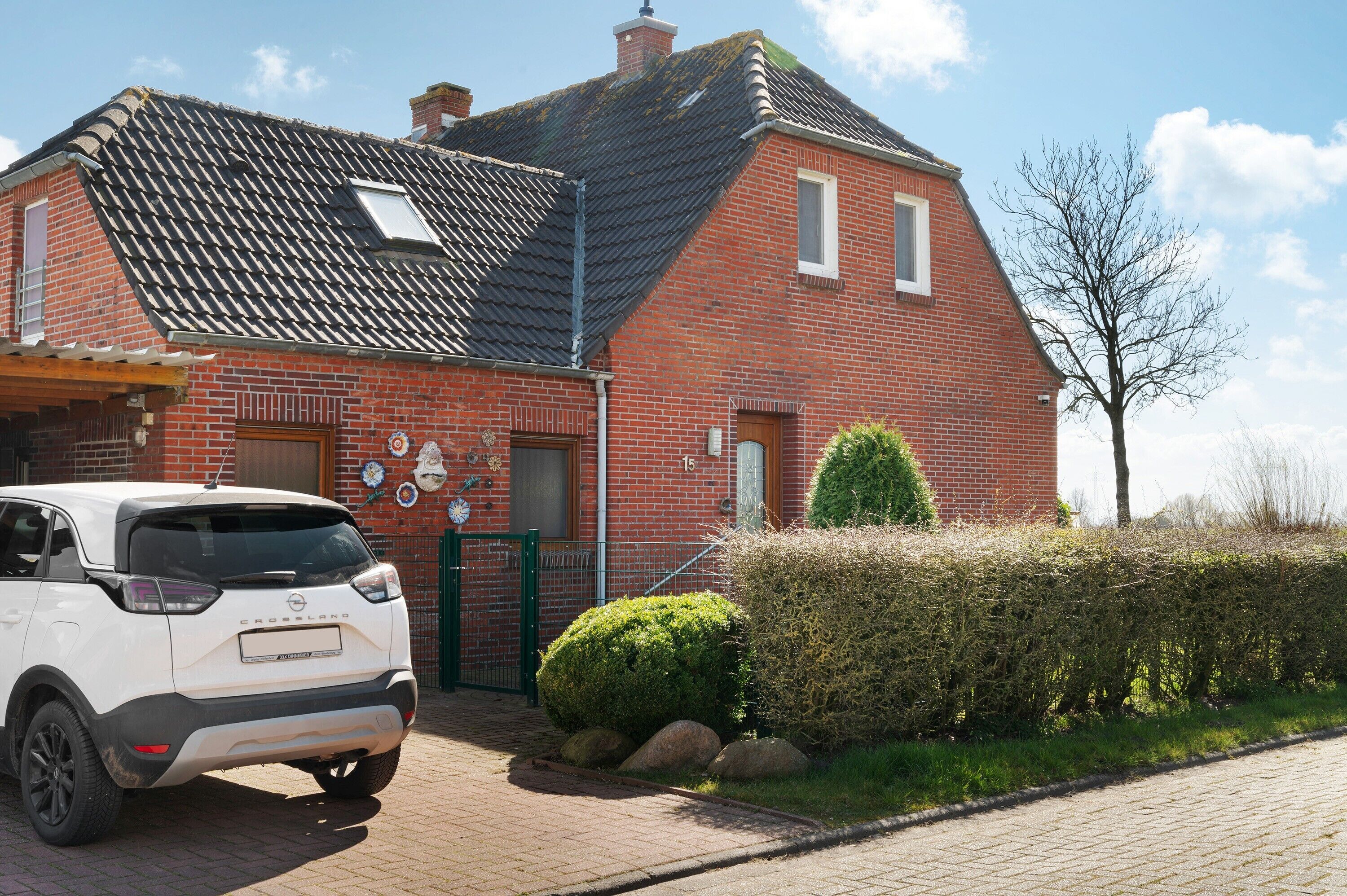 Een rode bakstenen woning met een pannendak, een witte auto geparkeerd ervoor, en een haag langs de oprit.
