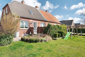 Une maison avec un toit en pente, une cheminée bien visible et une cour arrière clôturée avec un toboggan vert.