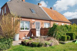 Une maison à deux étages, construite en briques, avec un toit en pente, une petite fenêtre et une porte d’entrée.