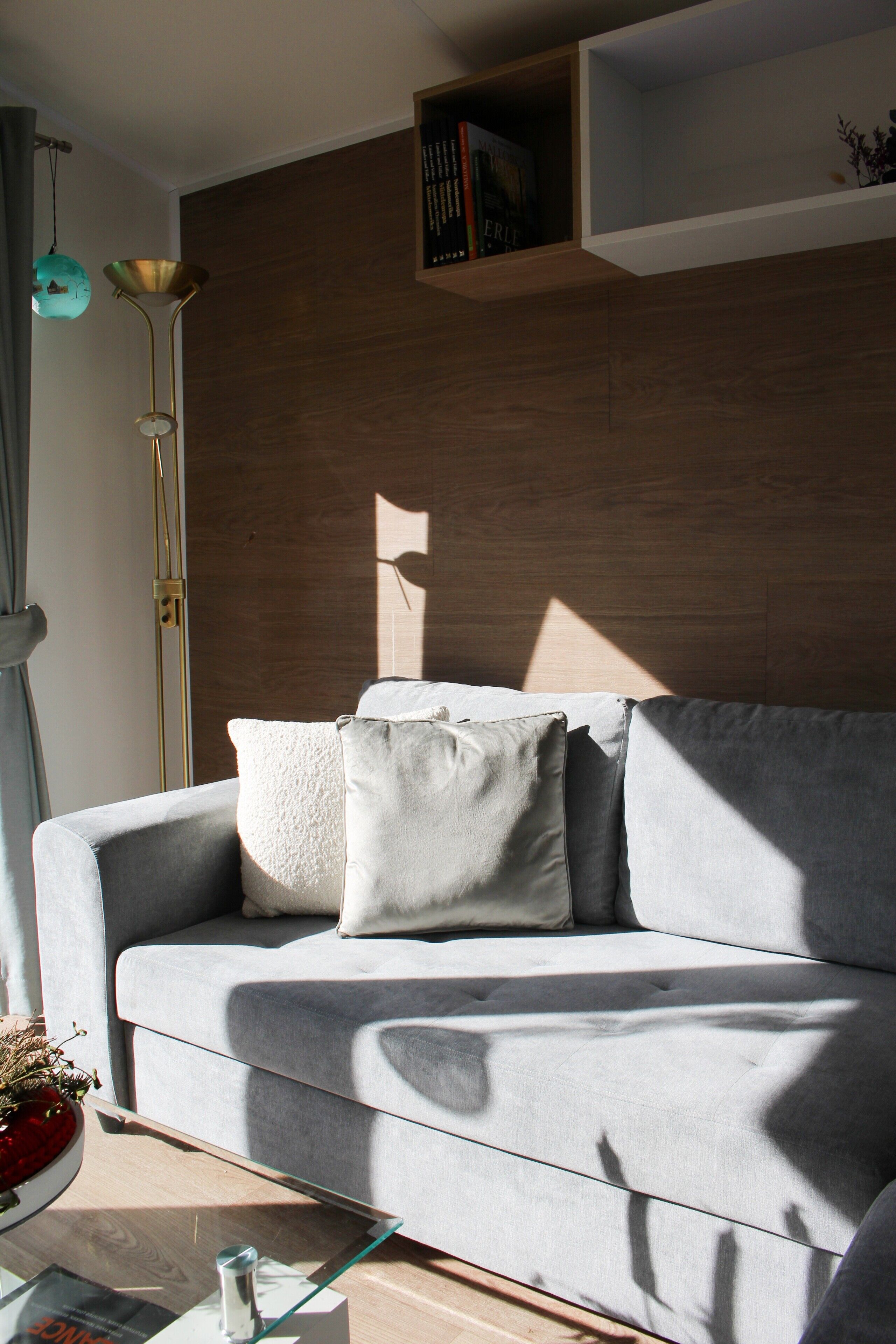 A modern living room with a grey sofa, a glass coffee table, and a wooden wall.