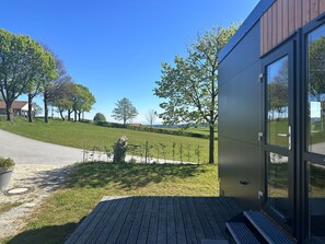 Ein modernes Gebäude mit einer Holterrasse, einer Steinskulptur und Blick auf eine grüne Landschaft mit Bäumen und einem fernen Berg.