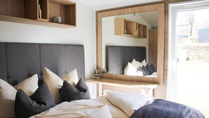 A bedroom with a large bed, a mirror, and built-in shelves. - Tiny Home 'Seppl' with Mountain View, Wi-Fi, and Air Conditioning (Untergriesbach)