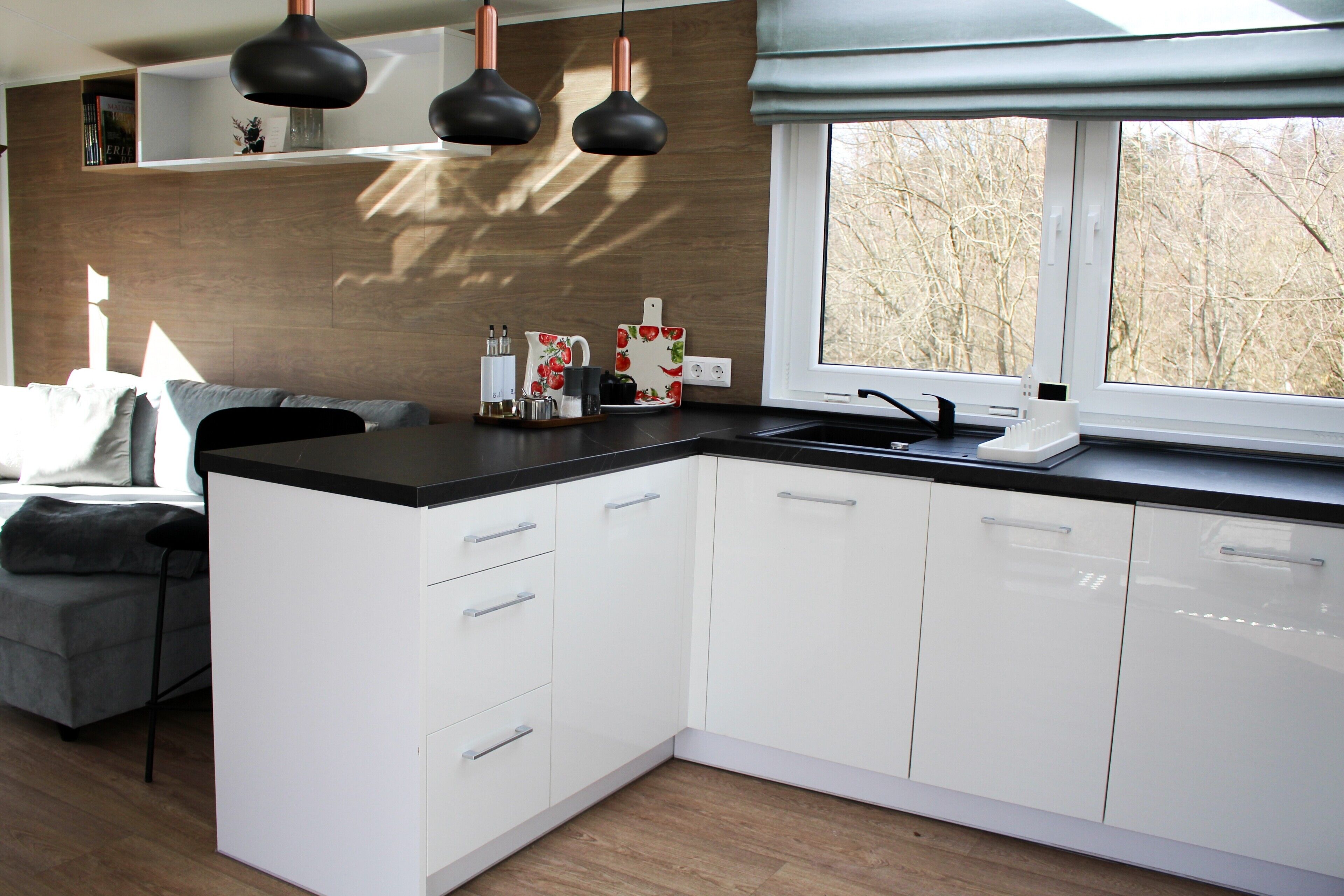 A modern kitchen with white cabinets, a black countertop, and a window with a view of trees.