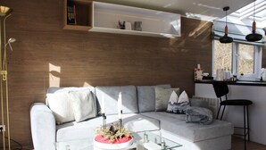 A modern living room with a glass coffee table, a sofa, and a bookshelf. - Tiny Home 'Seppl' with Mountain View, Wi-Fi, and Air Conditioning (Untergriesbach)