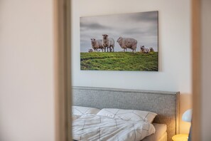 Camera da letto con un letto, una testiera, una lampada da comodino e un quadro appeso al muro raffigurante pecore.