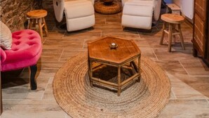 Une pièce chaleureuse avec un mur en pierre, deux fauteuils blancs, une table basse en bois, un pouf rose et un luminaire suspendu.
