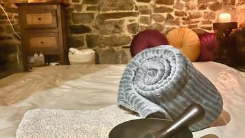 A stone-walled room with a bed, a wooden nightstand with a lamp, and a bowl with a pestle.