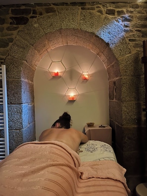A stone-walled room with a bed, a small table, and hexagonal wall sconces.