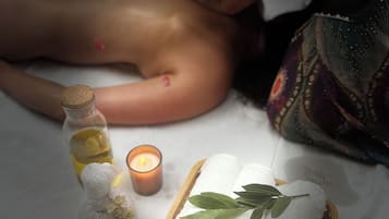 Une personne qui reçoit un massage, une bougie, une bouteille d’huile et un panier contenant des serviettes et des feuilles.