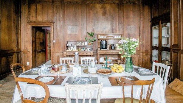 Un coin repas avec un mur lambrissé en bois, une table dressée pour quatre personnes et un vase rempli de fleurs.