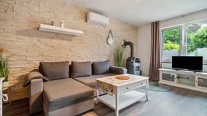 Ein modernes Wohnzimmer mit einem Ecksofa, einem Couchtisch, einem Fernseher auf einem weißen Schrank und einer Ziegelwand mit einer Klimaanlage.