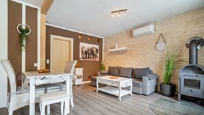 Ein Wohnzimmer mit einer Couch, einem Couchtisch, einem Esstisch mit Stühlen, einem Kamin und einer Wanduhr.