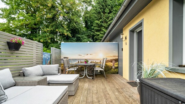 Eine Holzterrasse mit Gartenmöbeln, einem Tisch und Stühlen.
